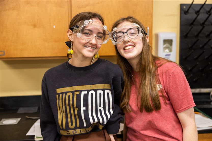 Two girls smile while wearing lab goggles